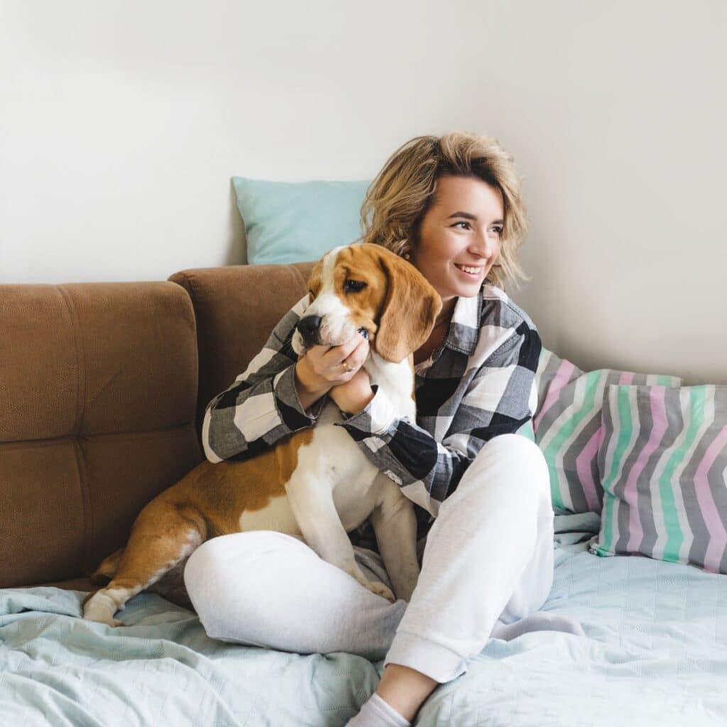 happy woman sitting on her couch with her dog smiling while holding the dog