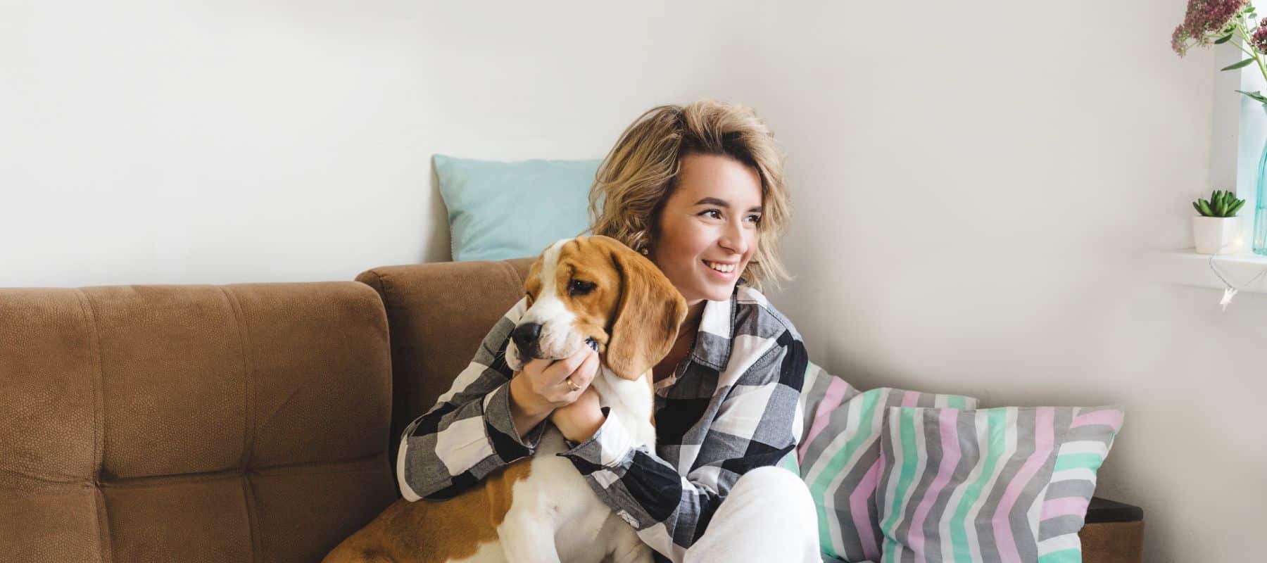 happy woman sitting on her couch with her dog smiling while holding the dog