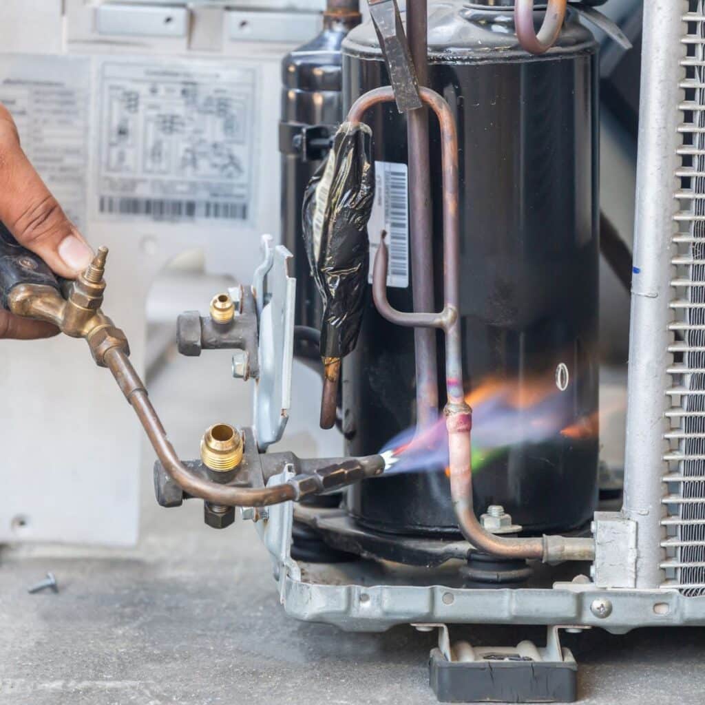 hvac tech using a torch to repair a line in a ac unit