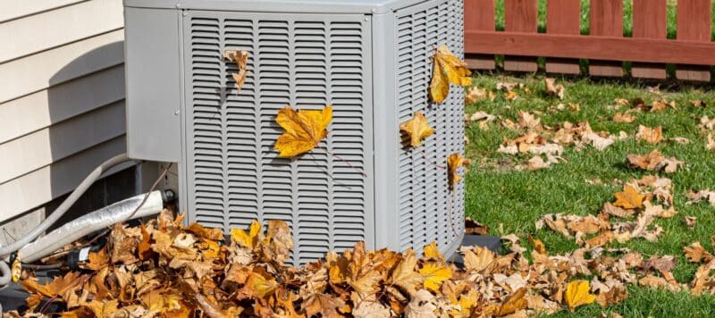 An outdoor HVAC unit surrounded by fallen autumn leaves, highlighting the need for seasonal maintenance