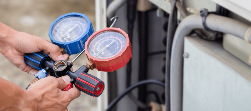 A technician uses a red and blue gauge manifold set to check and adjust refrigerant levels on an HVAC system