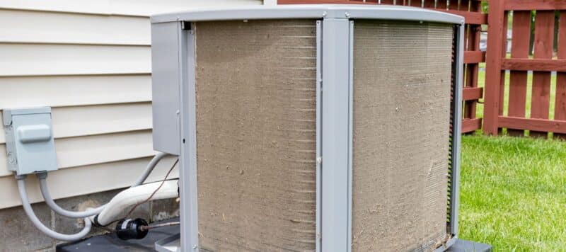 Outdoor HVAC unit with heavily dust-covered coils, indicating poor maintenance and potential airflow restriction